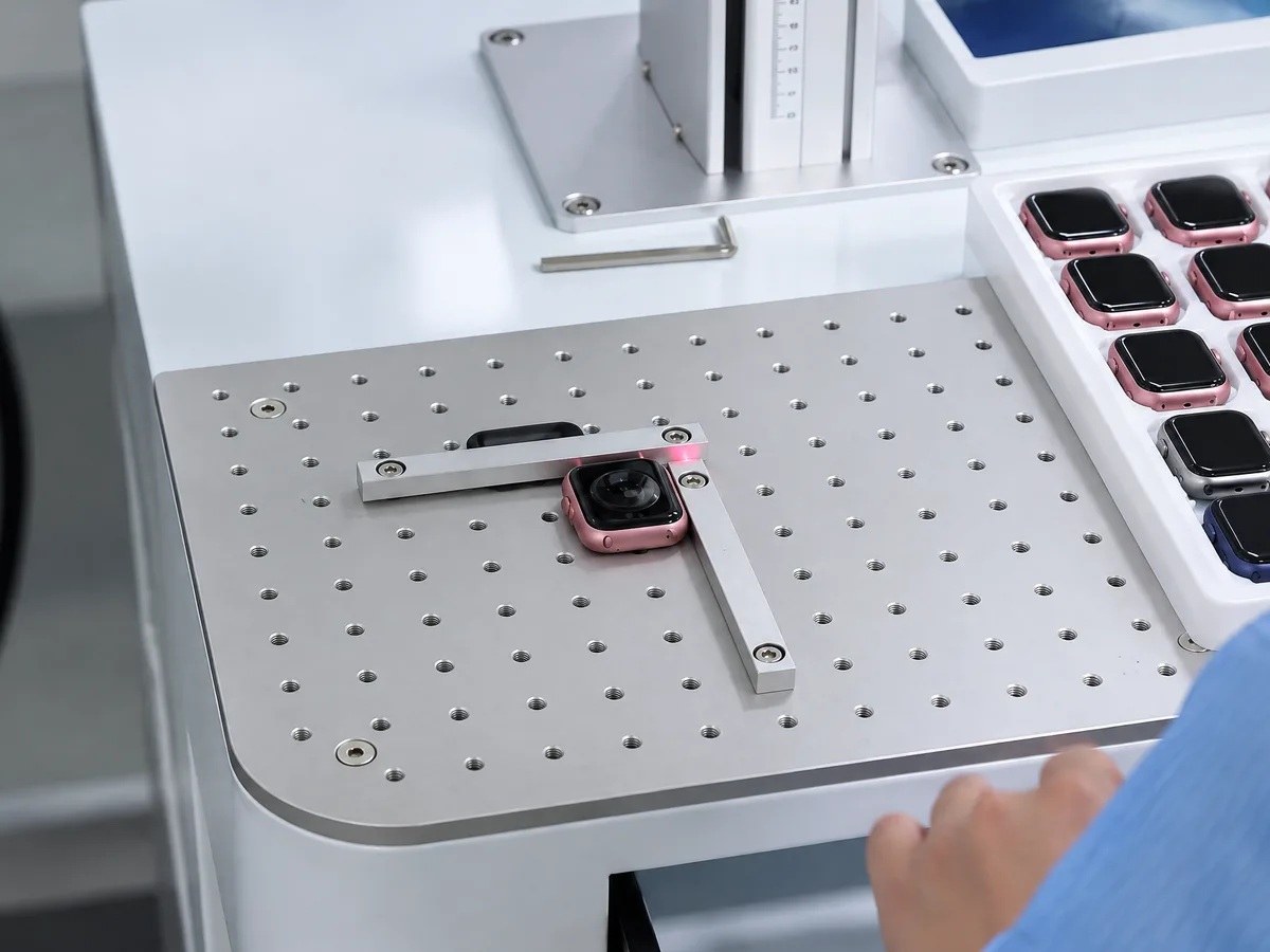 A smartwatch under red-light inspection on a perforated quality-control bench